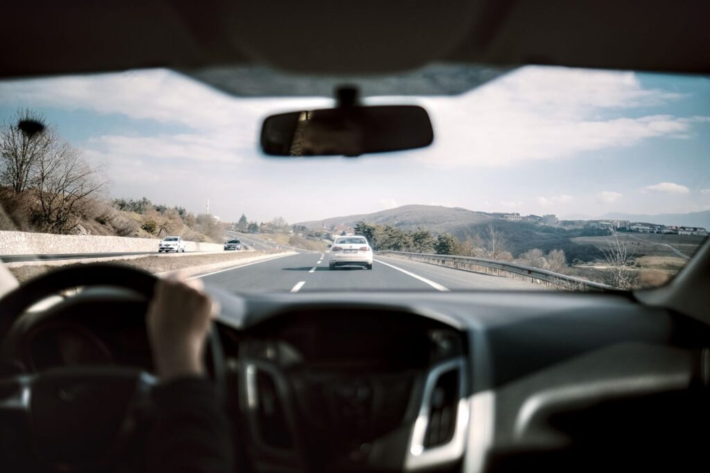 Automóvil circulando por carretera con colinas al fondo.