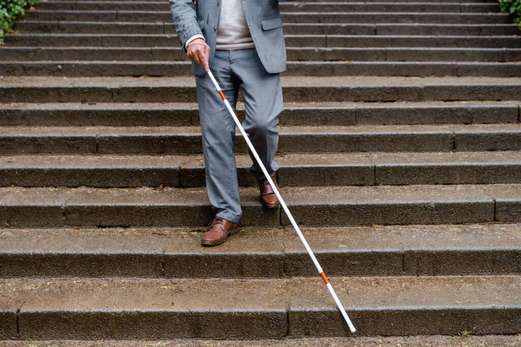 Blind man using white cane descending outdoor stairs.