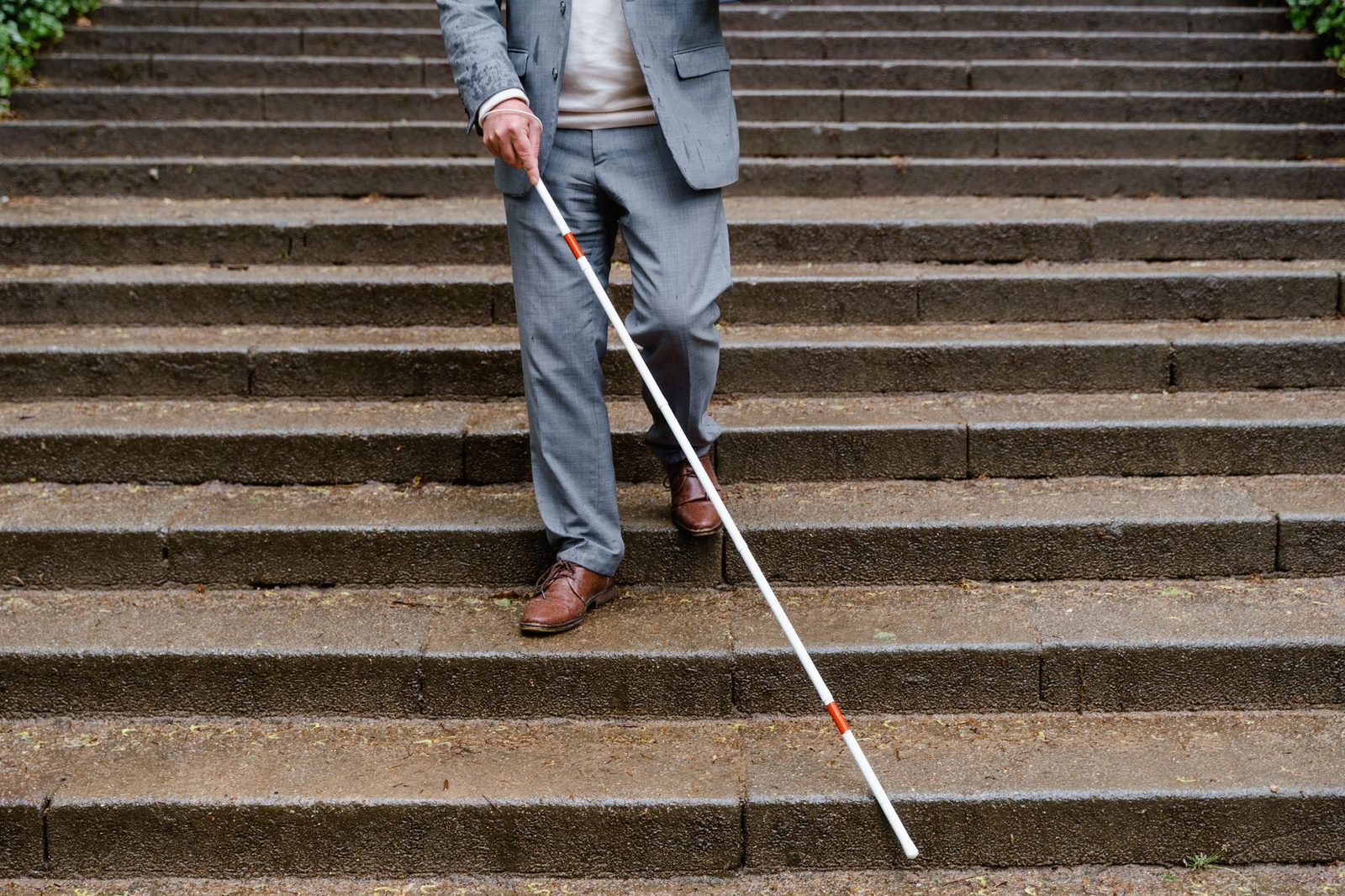 Blind man using white cane descending outdoor stairs.