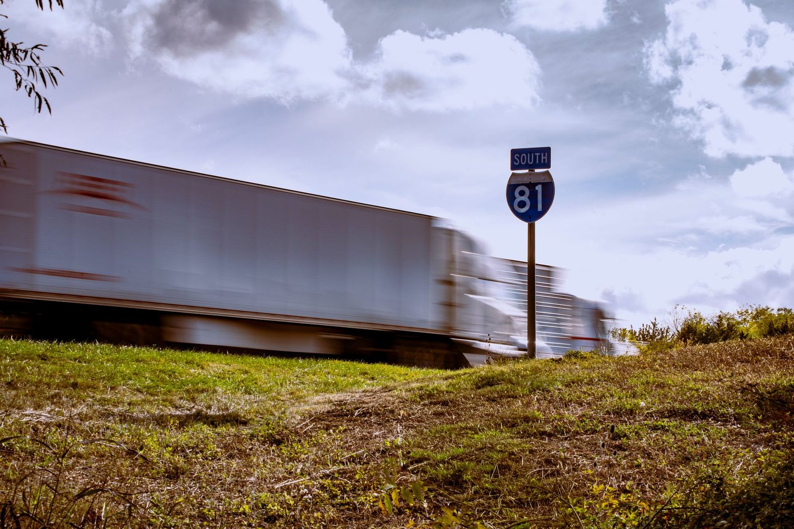 Blurred truck driving on interstate highway with clear blue sky and grass median.