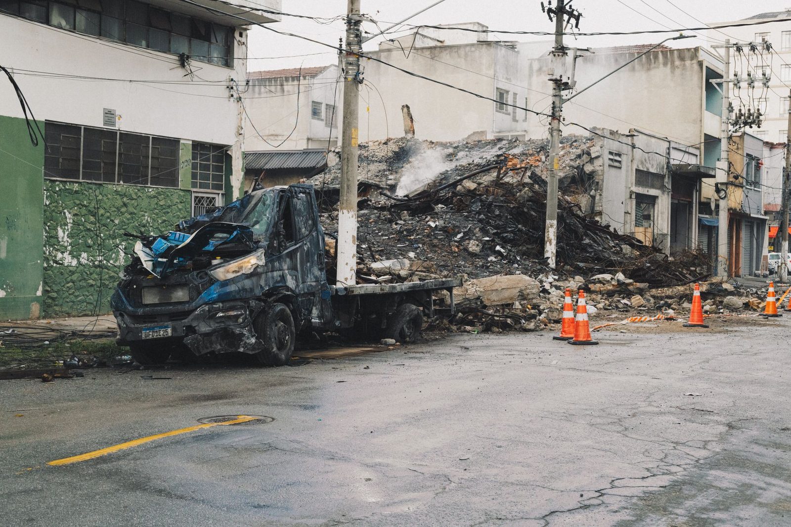 Burned-out vehicle and debris scattered on city street after fire.