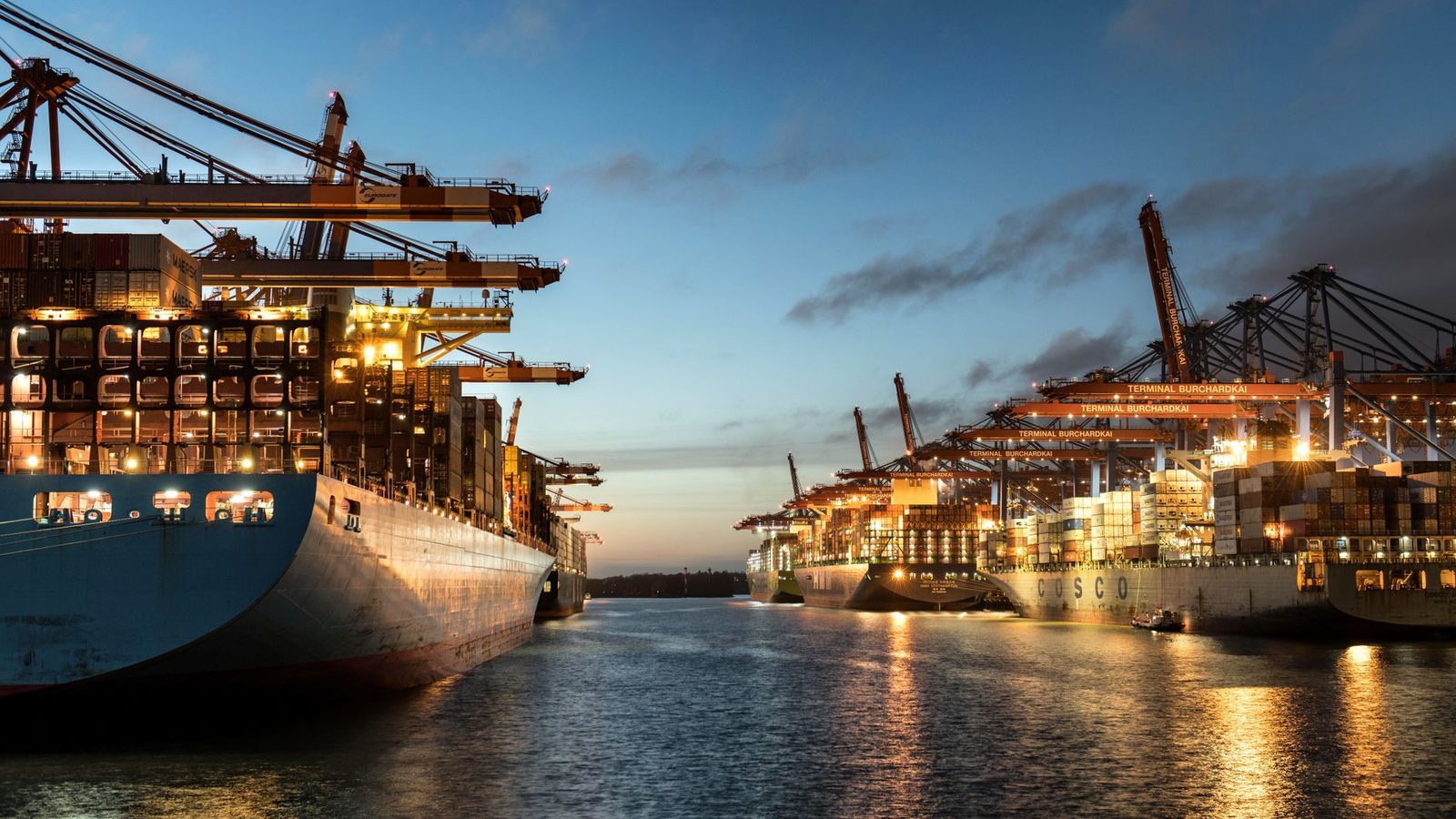 Container ships moored at Hamburg harbor at sunset, representing maritime shipping operations.