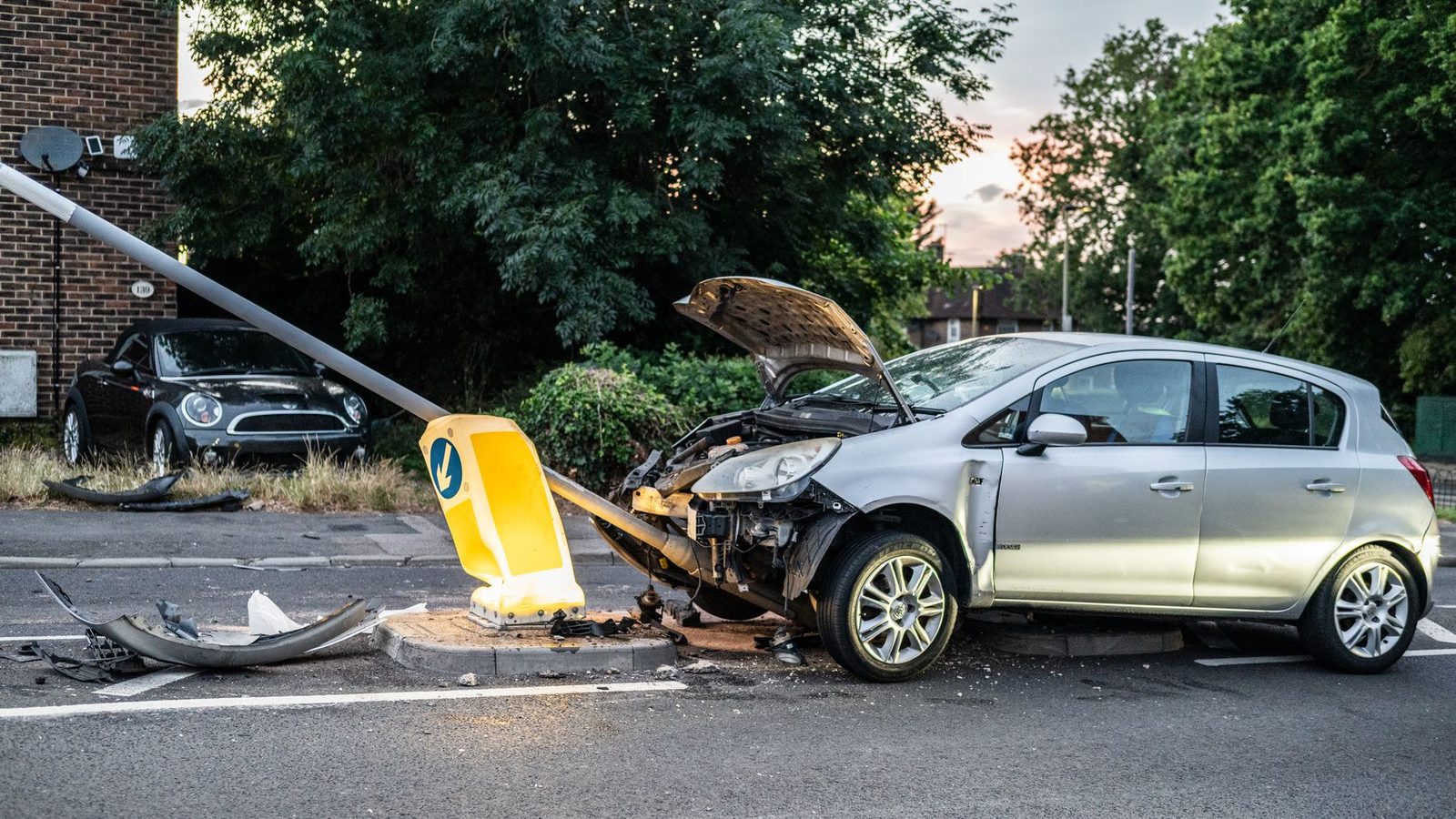 Damaged car crashed into street lamp post during evening.