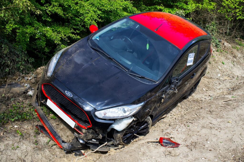 Damaged red and black Ford Fiesta abandoned off-road after accident.