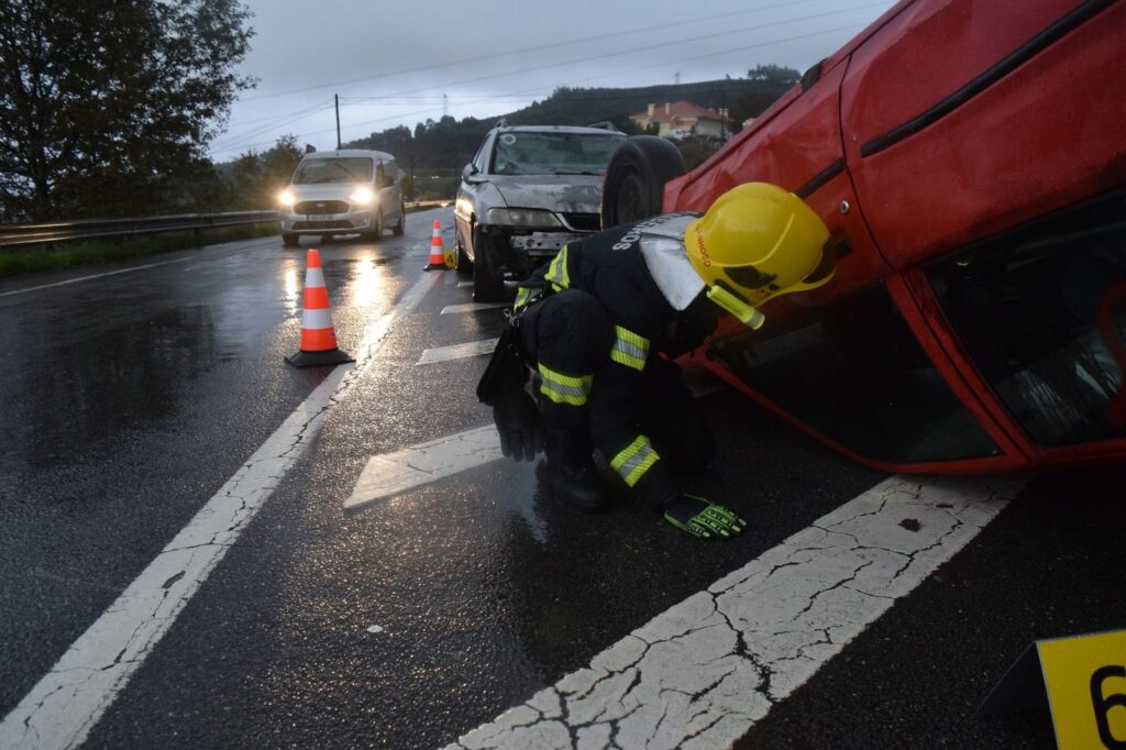 Firefighter assisting at overturned vehicle on wet road during emergency response.