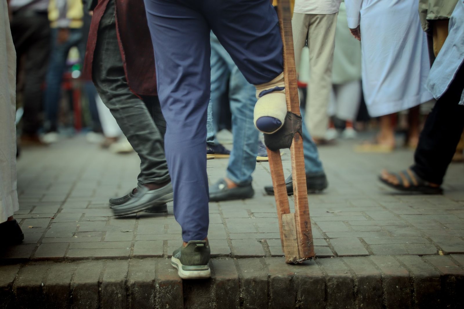 Hombre con discapacidad usando muleta casera para navegar una calle concurrida de la ciudad.