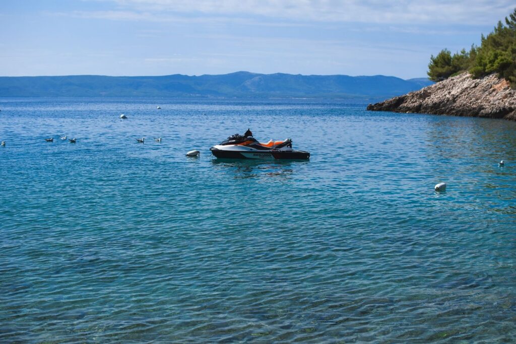Jet ski parked on calm blue water near rocky coastline.