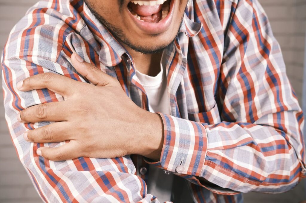 Man in plaid shirt holding his shoulder in pain.