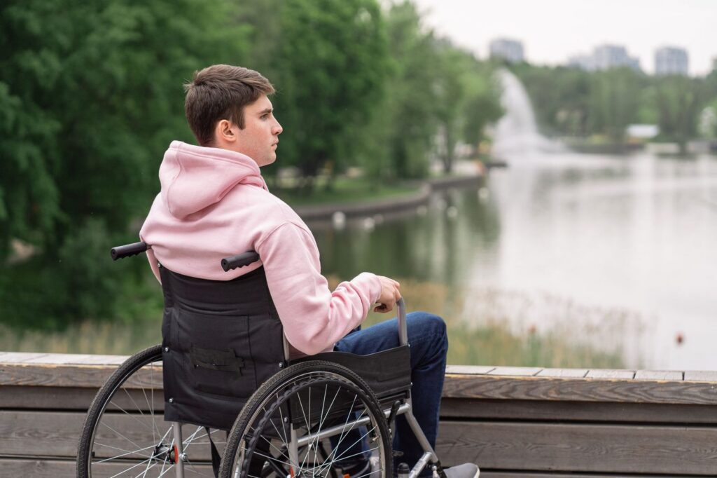 Man in wheelchair looking out over a calm lake in reflection.