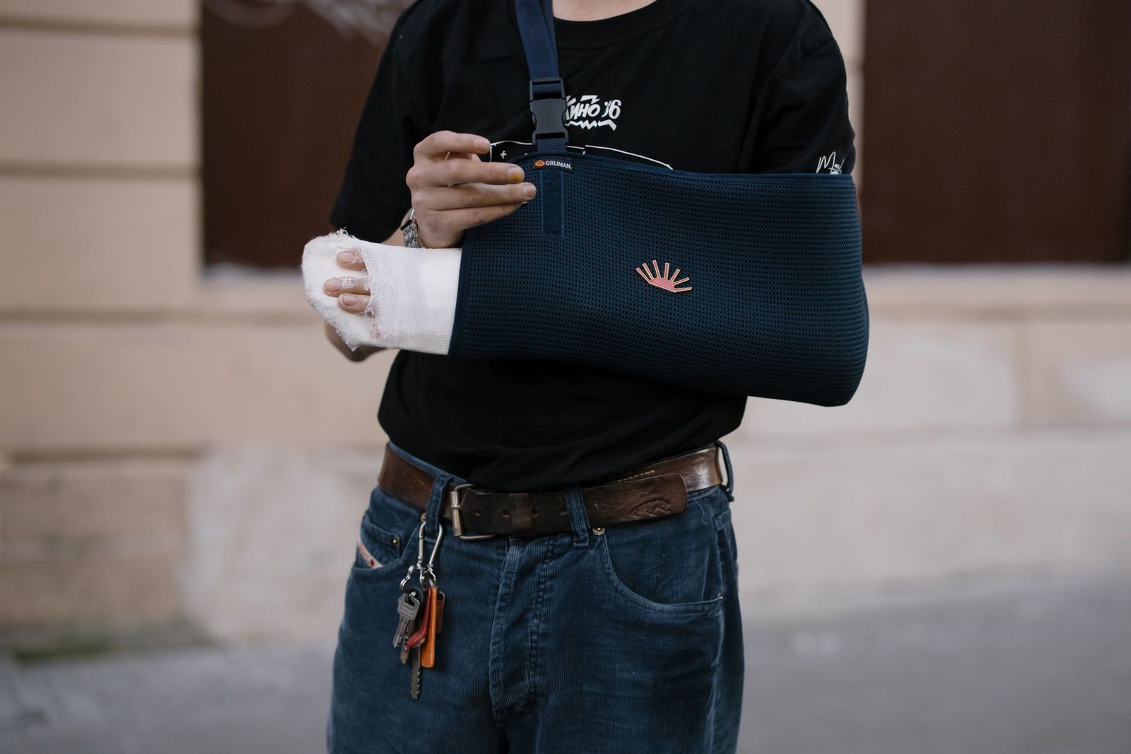 Man with arm in dark sling and bandage standing outdoors.