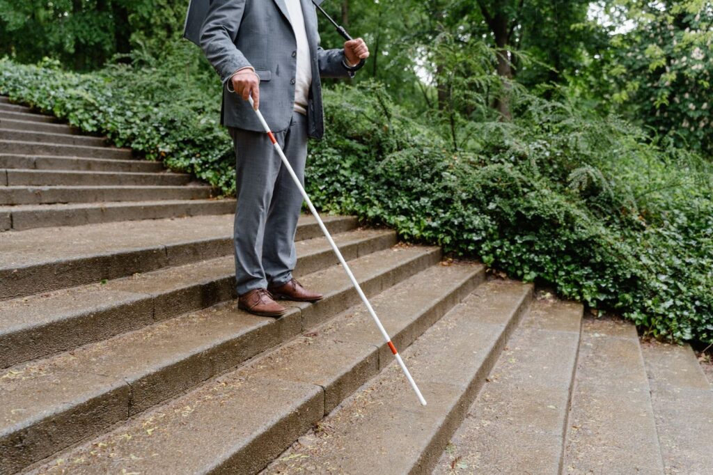 Man with white cane navigating outdoor concrete stairs independently.