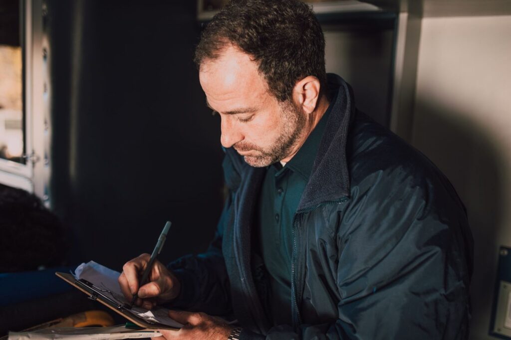 Man writing notes on clipboard, focused expression.
