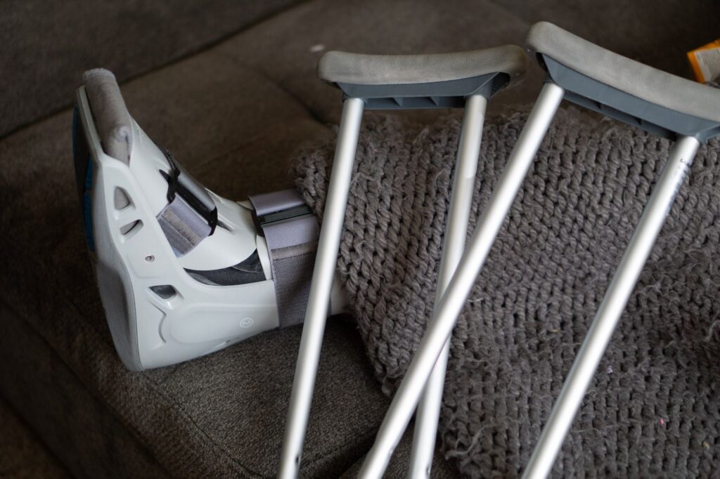 Orthopedic boot and crutches on a couch representing home injury recovery.
