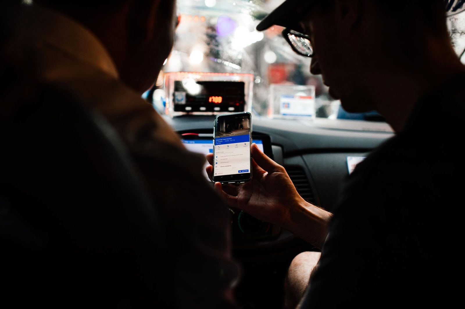 Passengers checking directions on smartphone inside car at night.