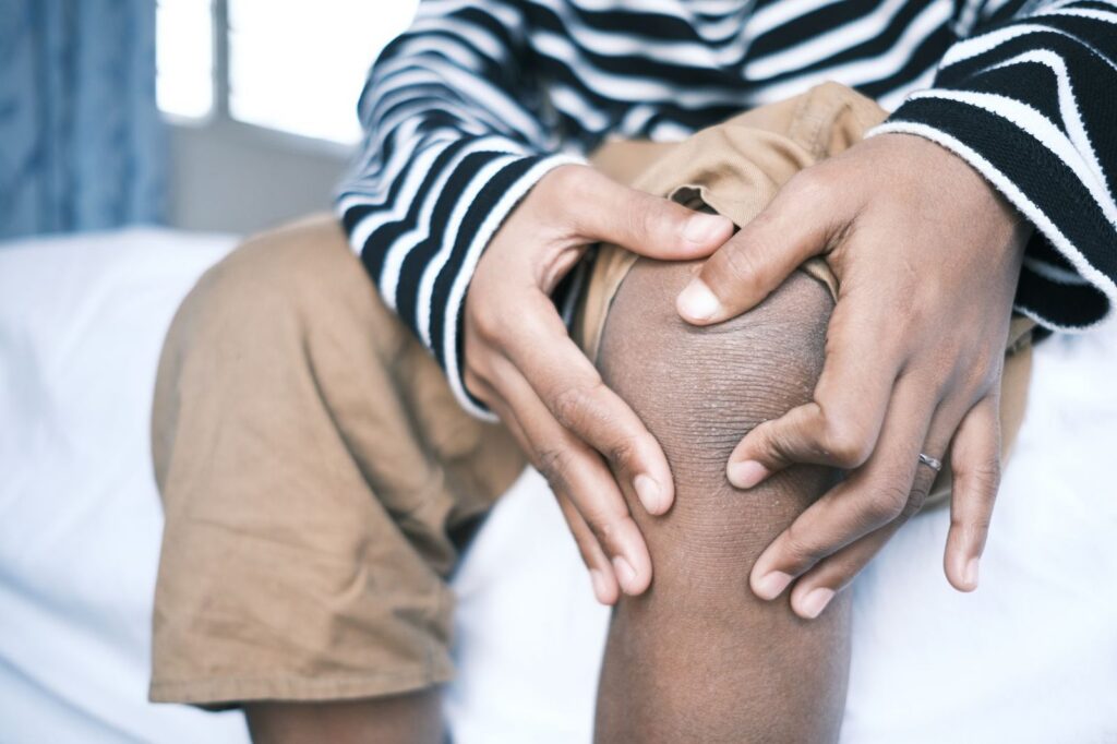 Person holding their knee in pain, wearing striped clothing.