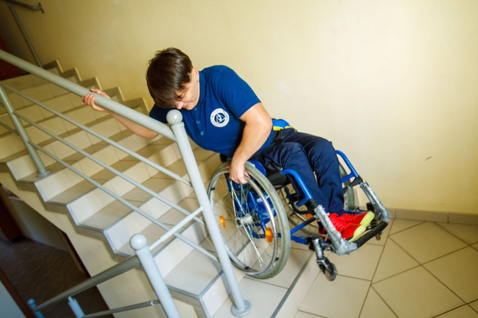 Person in wheelchair approaching indoor stairs with handrail, illustrating accessibility barriers.