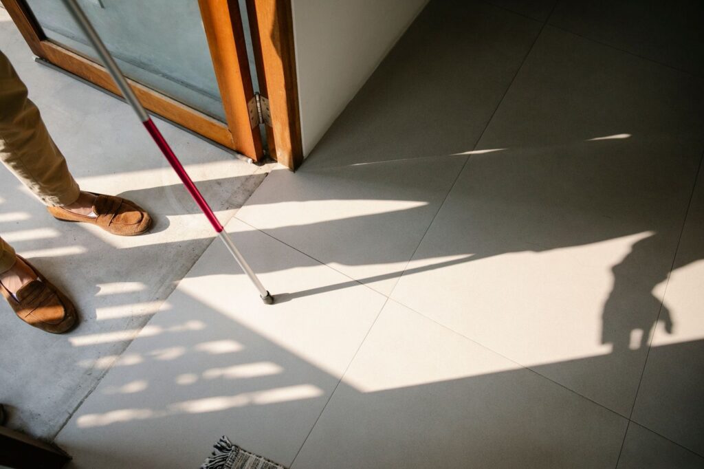 Senior person with walking stick entering bright room with tiled floor.