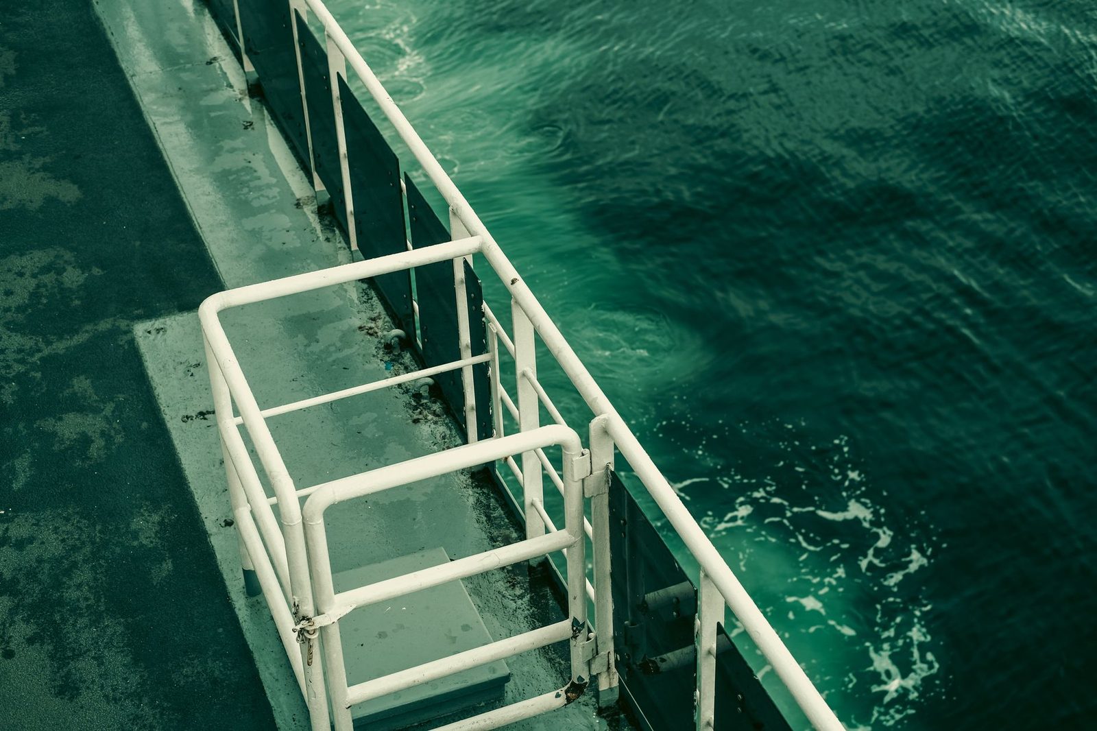 Ship's railing overlooking calm green ocean water.