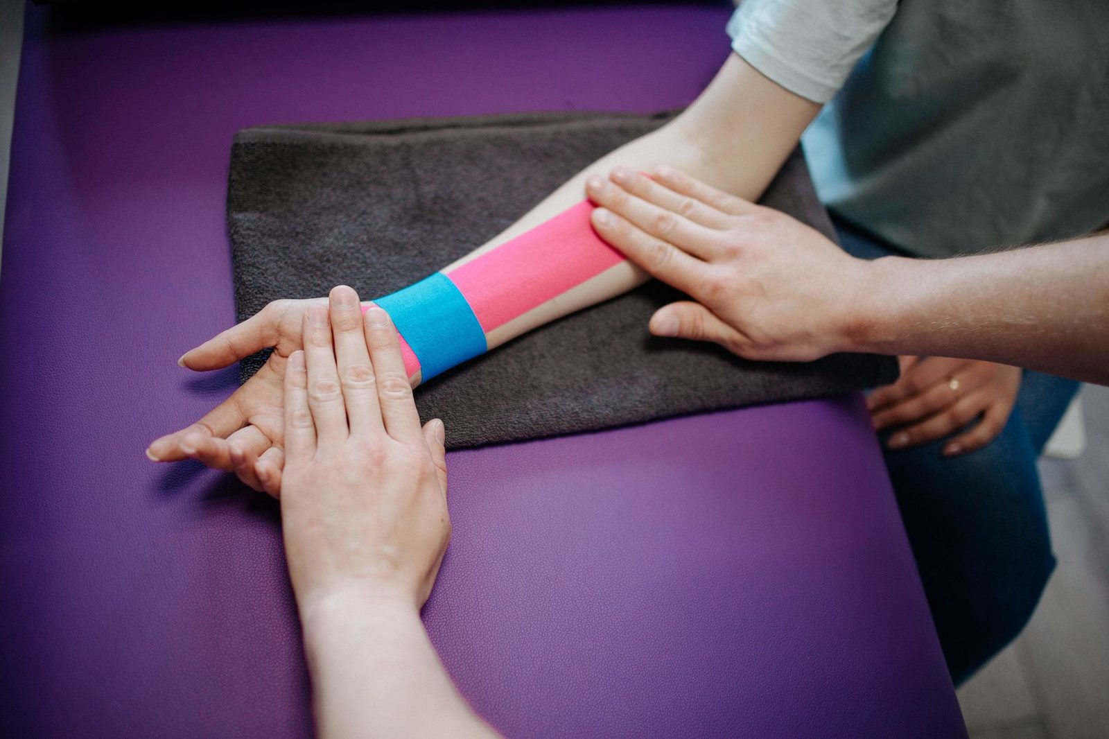 Therapist applying kinesiology tape to patient's forearm for elbow support and recovery.