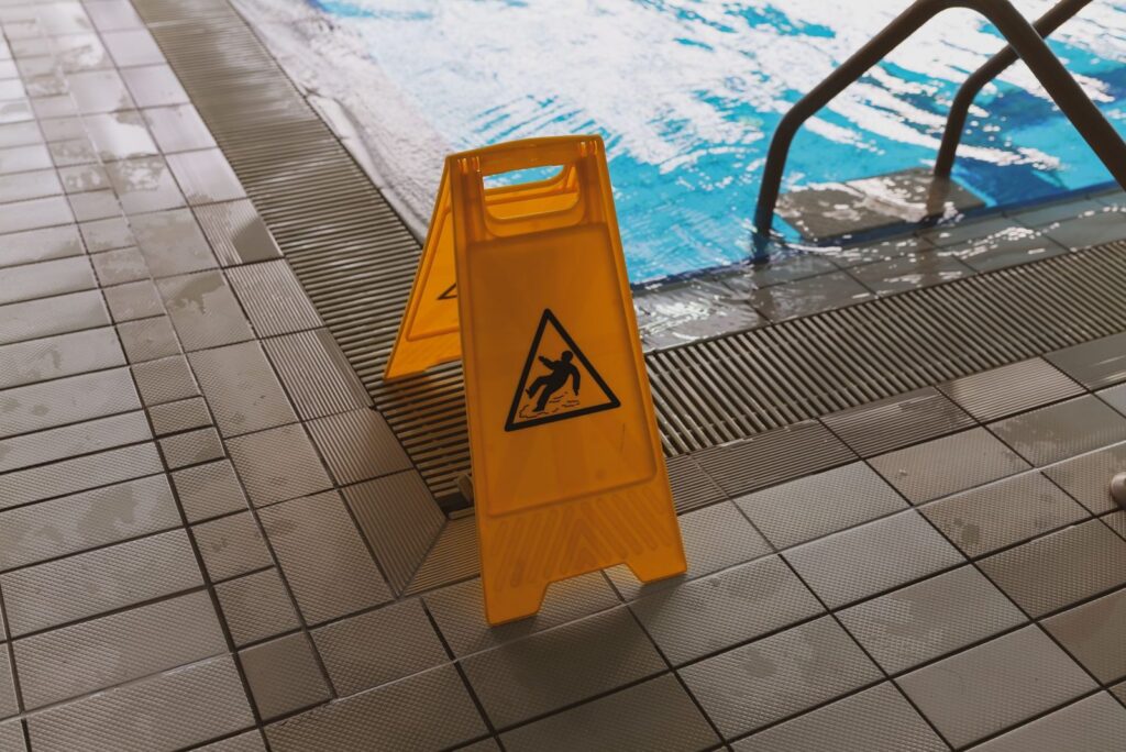 Wet floor caution sign placed beside a swimming pool.