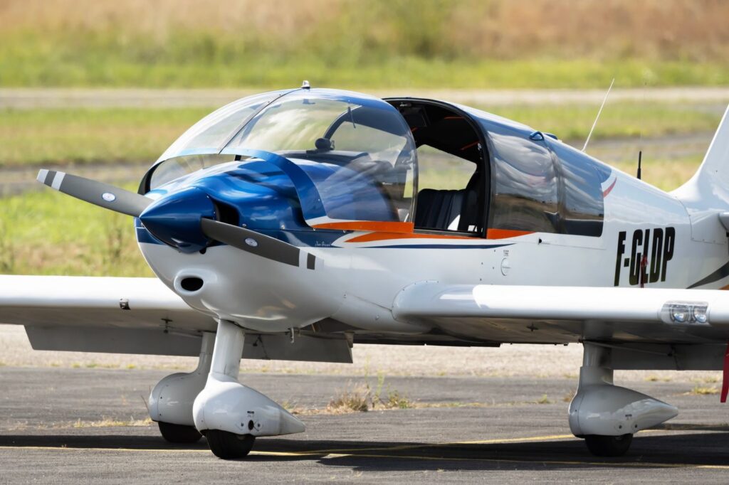 White and blue light aircraft with open canopy on tarmac.
