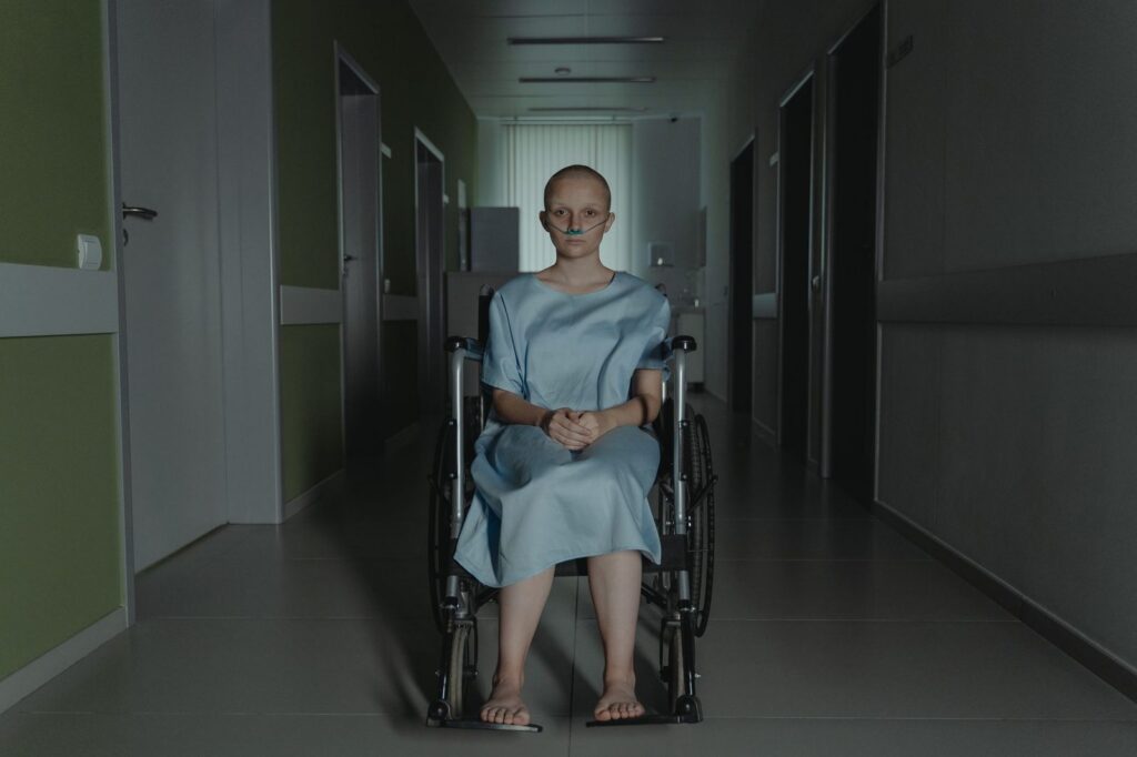Woman in wheelchair in hospital corridor wearing medical gown.