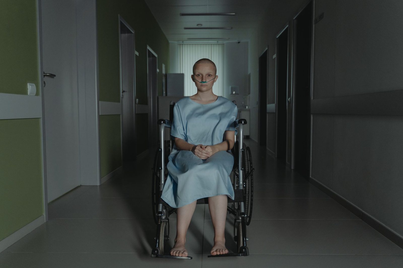 Woman in wheelchair in hospital corridor wearing medical gown.