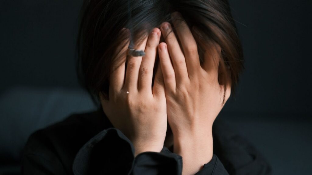 Woman with hands covering face, appearing stressed and overwhelmed indoors.