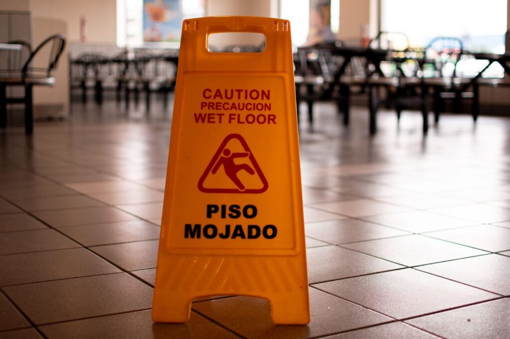 Yellow wet floor caution sign on tiled cafeteria floor.