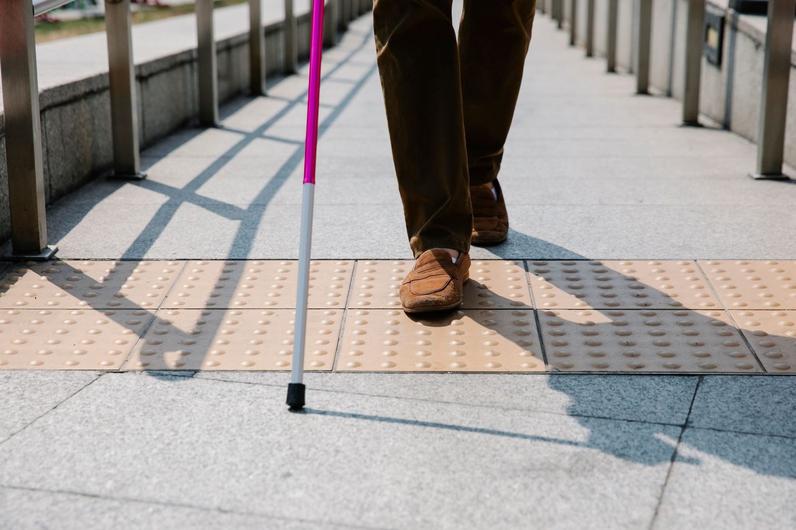 A close-up of a person's hand gripping a walking cane on tactile paving outdoors.