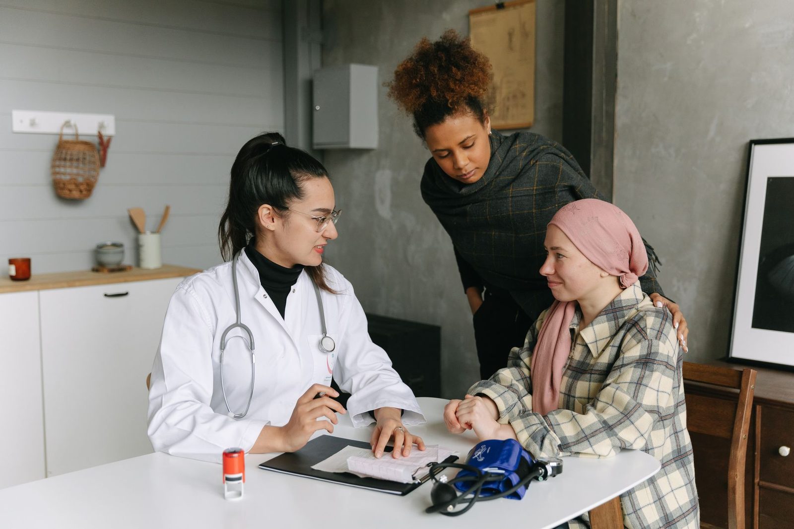 A doctor talks with a cancer patient and a friend in a home setting, offering support.