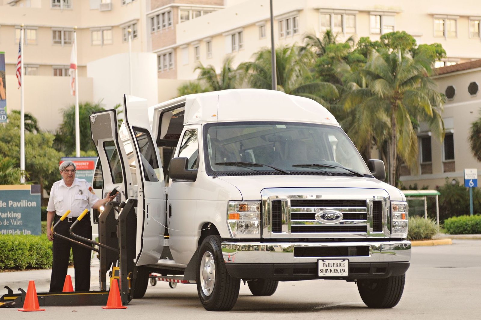 Accessible van with a wheelchair lift and a driver assisting a passenger at a city curb.