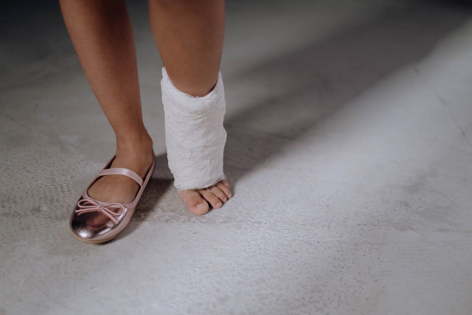 Child's leg in orthopedic cast with pink shoe on concrete floor.