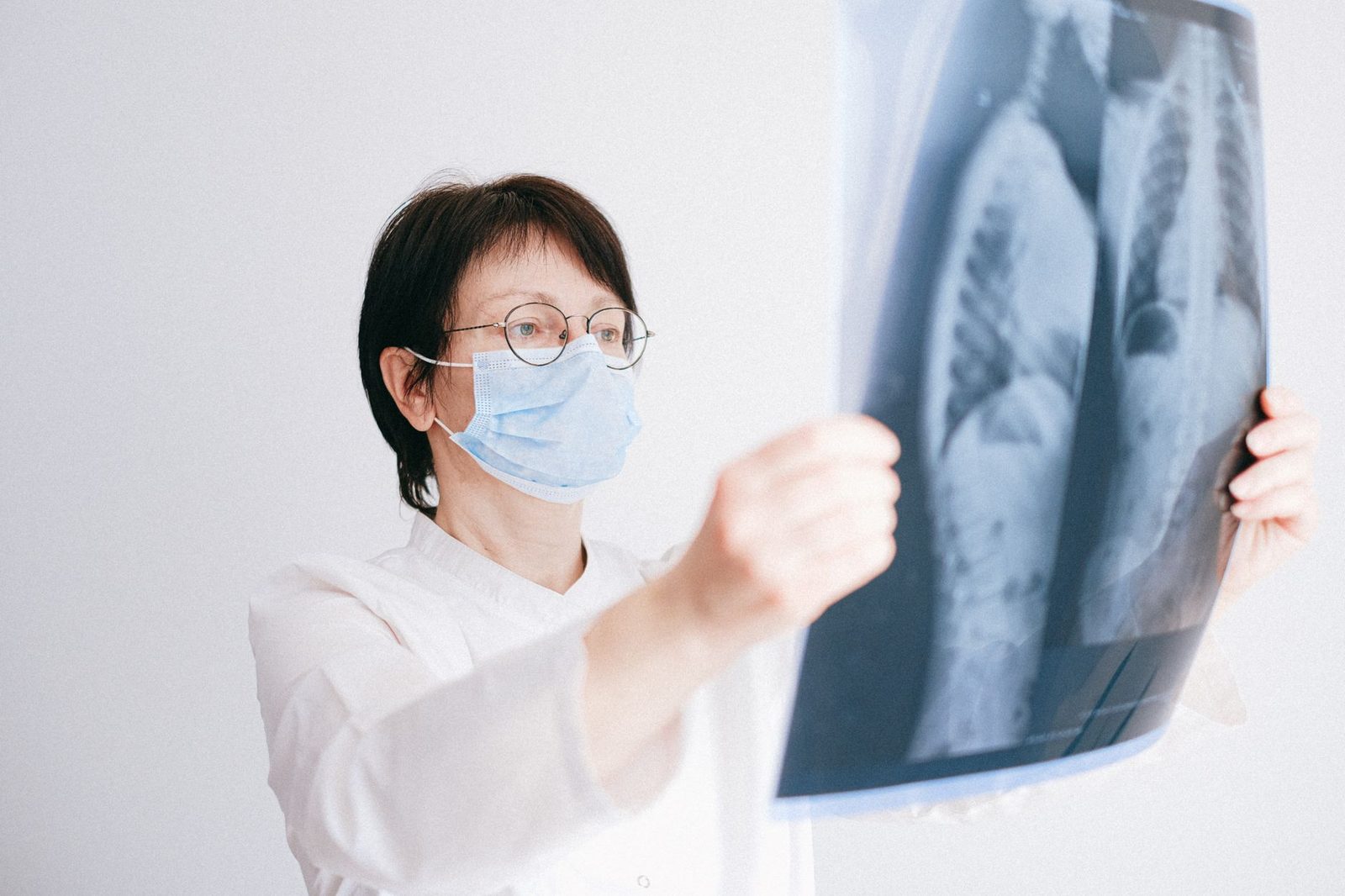 Doctor in a face mask studying a lung x-ray in a clinical examination room.