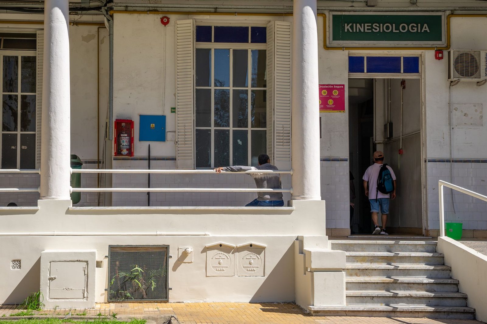 Edificio de kinesiología con arquitectura vintage y personas entrando.