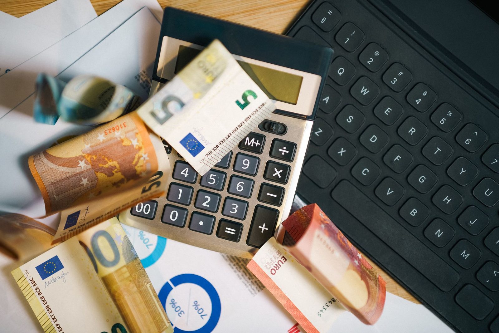 Euro banknotes, a calculator, and a laptop keyboard arranged on a desk for financial analysis.