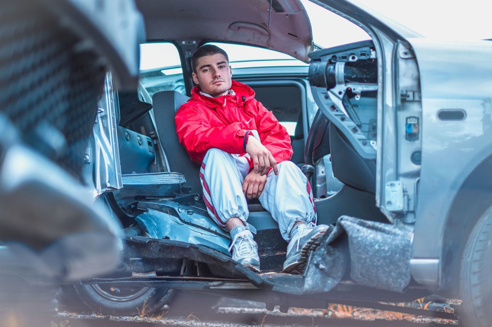 Hombre joven en chaqueta roja dentro de auto dañado tras accidente vehicular.