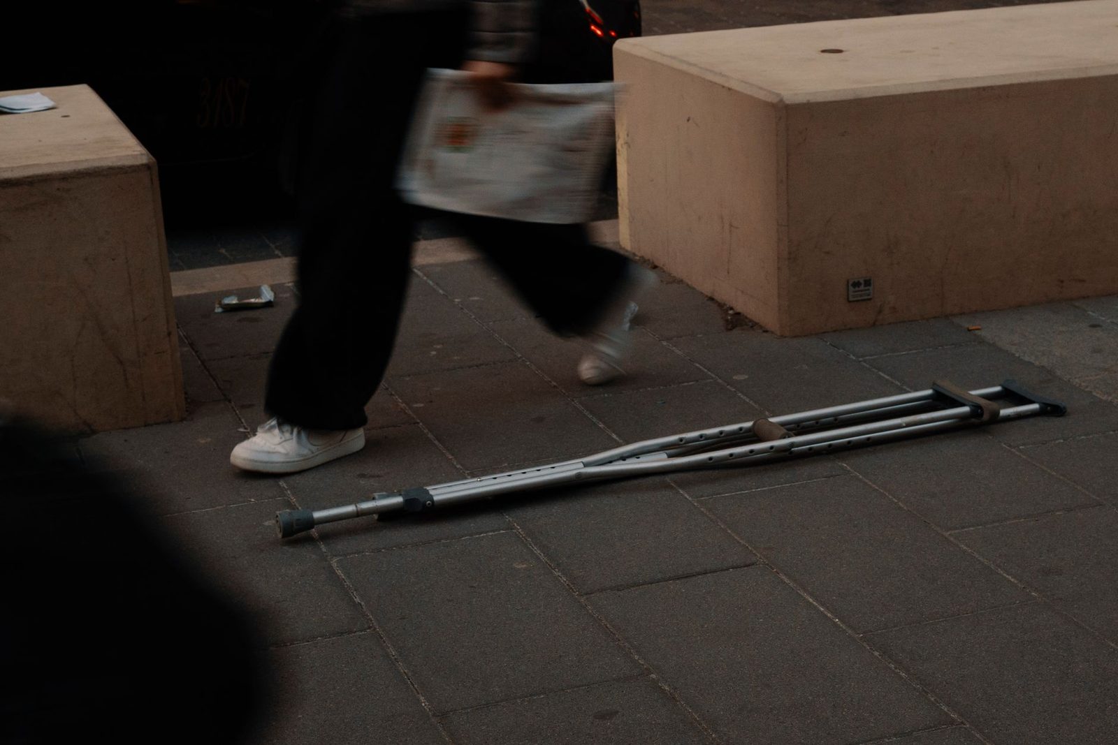 Muletas abandonadas en acera urbana con peatones de fondo.