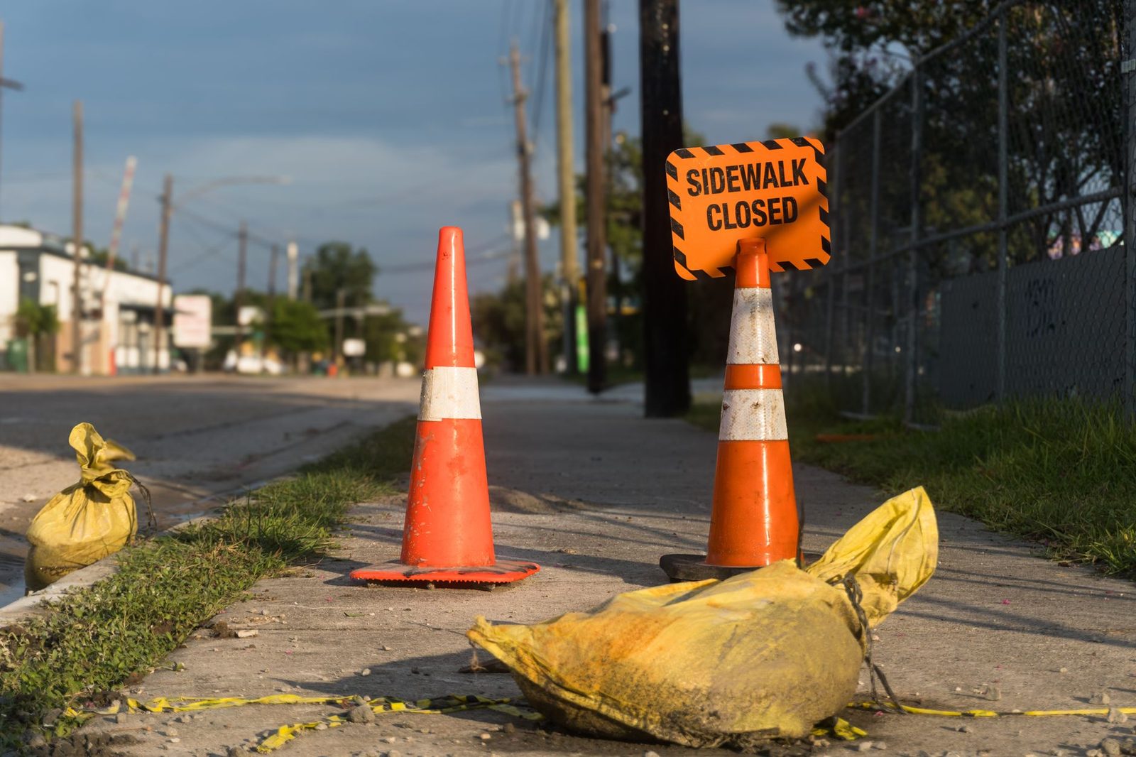 Orange traffic cones and a closed sidewalk sign line an urban street in Houston.