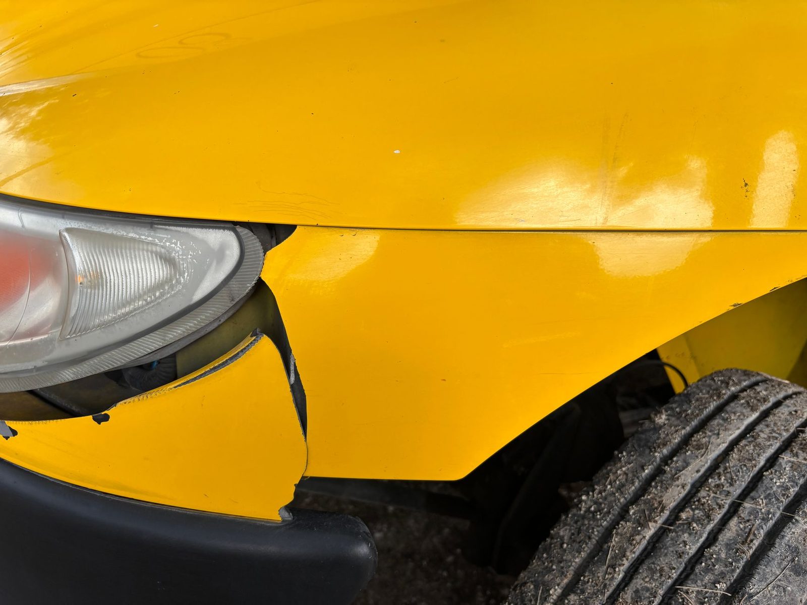 Parachoques amarillo dañado y faro roto de automóvil en accidente.