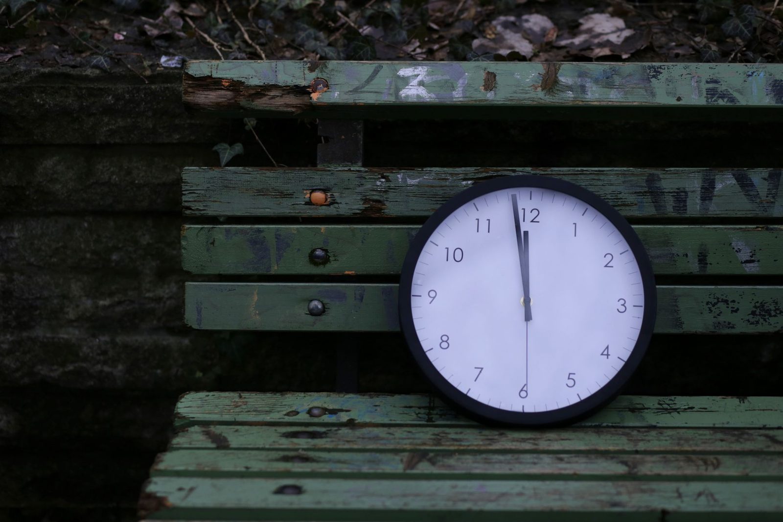 Reloj analógico sobre banco de madera verde rústica al aire libre.