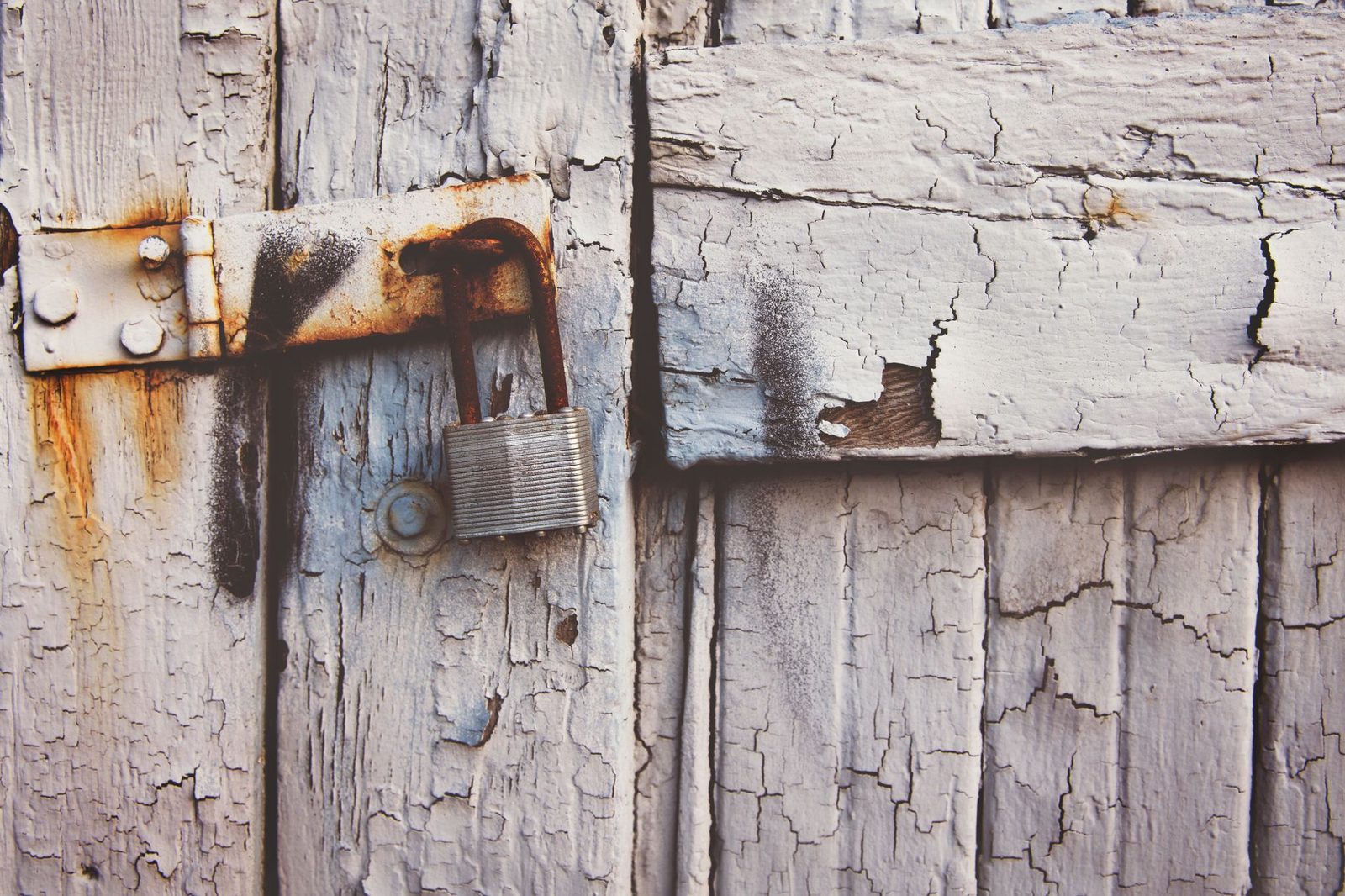 Rusty padlock on weathered wooden door with peeling paint.