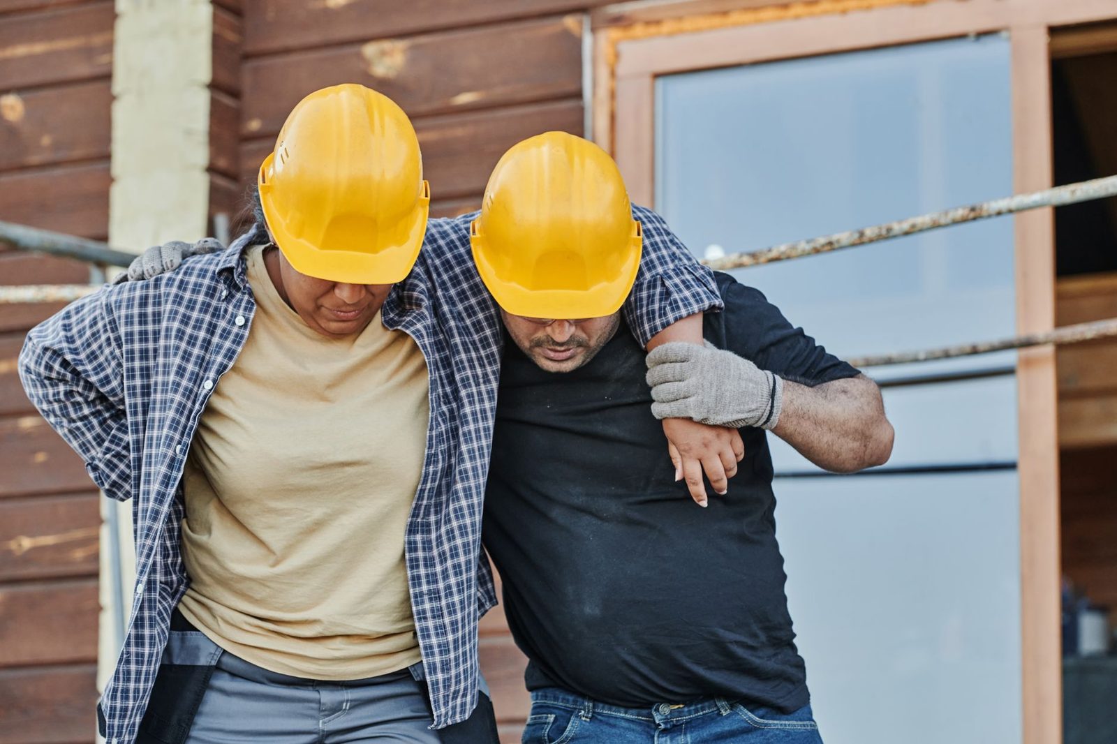Two construction workers in hard hats assisting each other at a building site.
