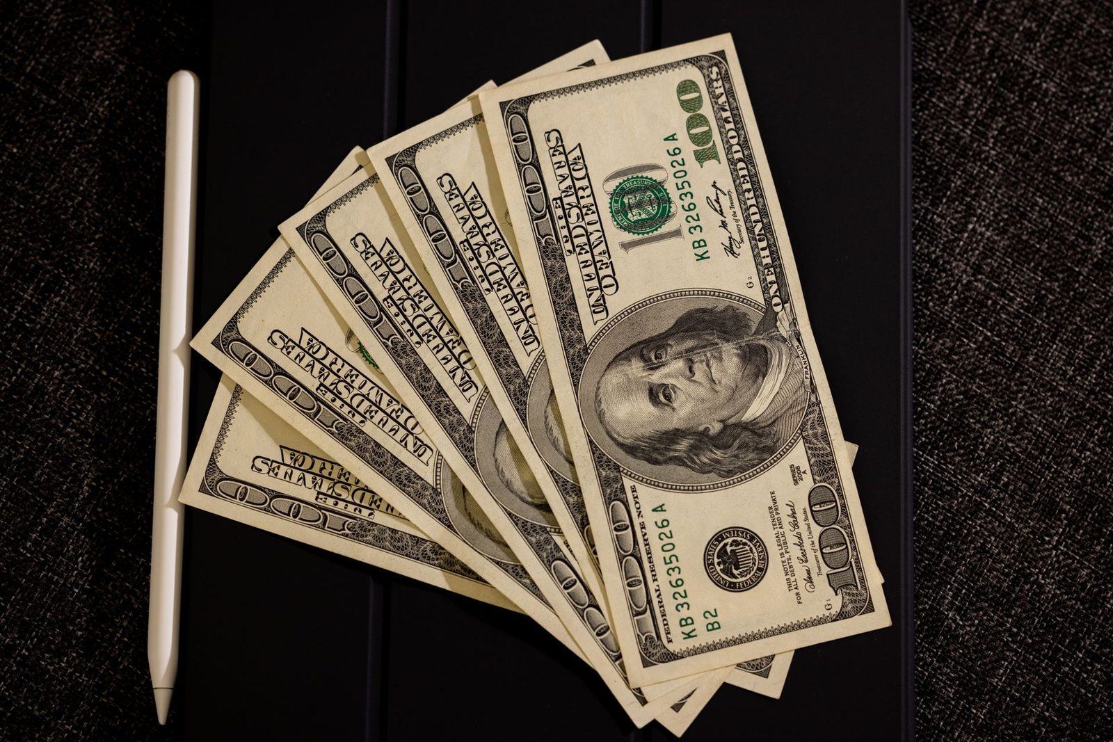 US dollar bills and stylus on black surface representing financial compensation.