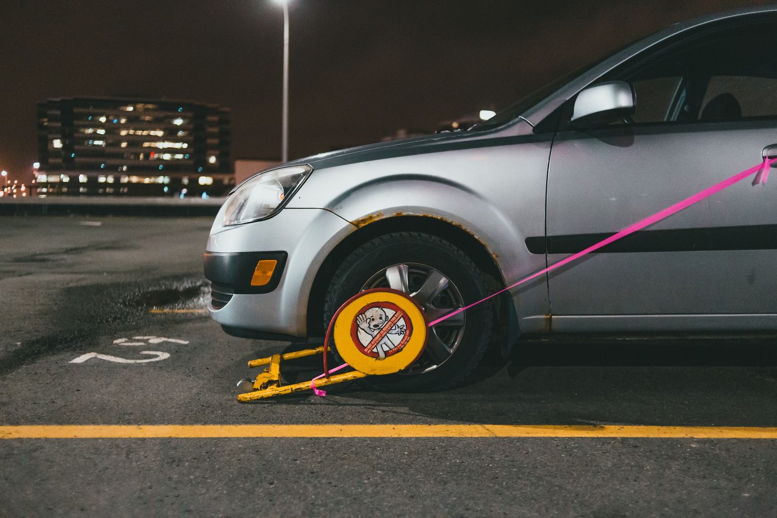 Wheel-clamped silver car in dark parking lot at night.
