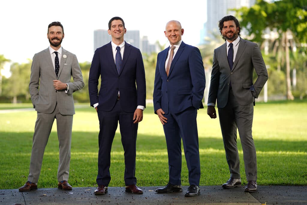 Four smiling men in suits outdoors