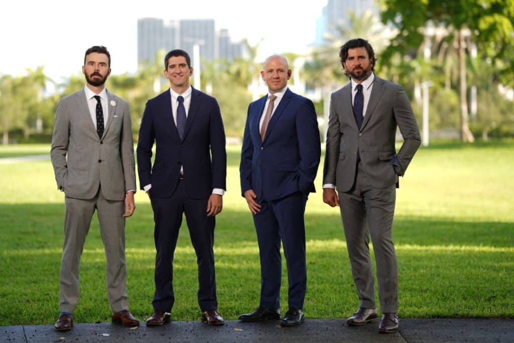 Four smiling men in suits outdoors